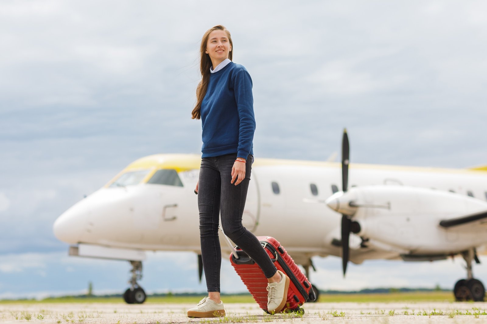 Young Woman Traveler with Red Luggage Walking at Airport Before Vacation Flight Near Airplane